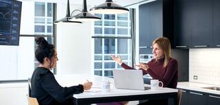 A diverse group of professionals discusses ideas at a modern conference table, with laptops and documents scattered around.