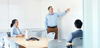 A modern office space shows several people working at computers, sunlight streaming in, highlighting a productive atmosphere with city views.