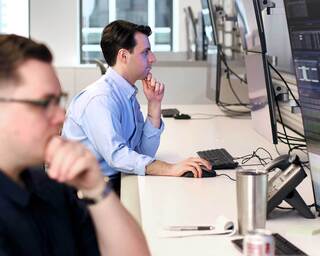 A middle-aged man in a blue shirt gestures at a desk.