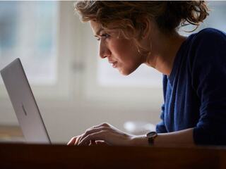 A focused woman works intently on a laptop, showcasing concentration and engagement in a serene indoor setting.
