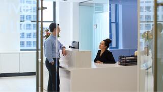 A man in a white shirt discusses ideas intently with two women during a meeting, fostering collaboration in a well-lit, modern space.