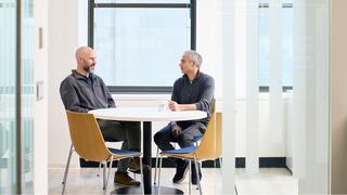 Two men engage in a lively conversation at work, sharing smiles and ideas in a bright, modern office setting.